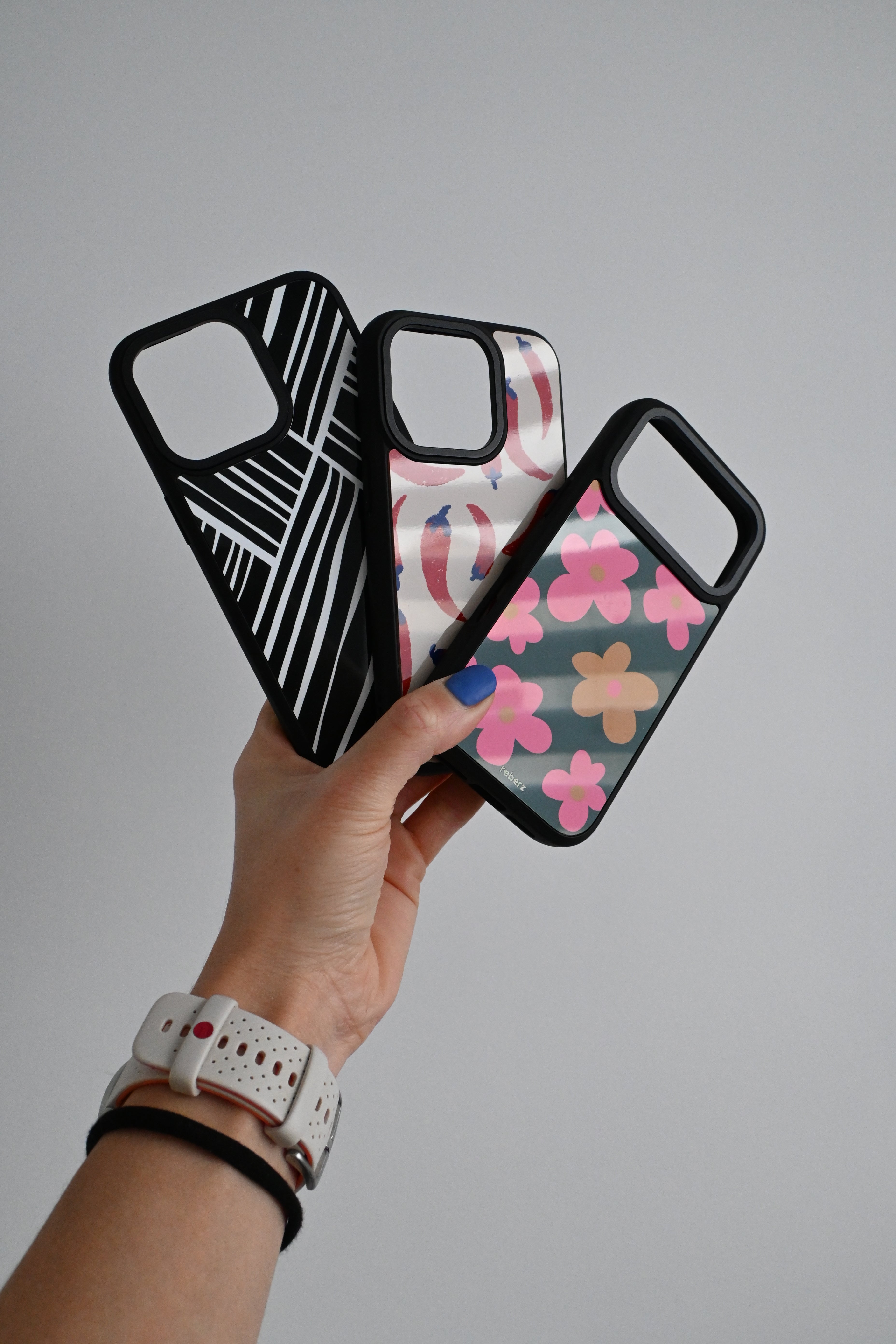 Hand holding two phone cases with geometric and floral designs on a gray background
